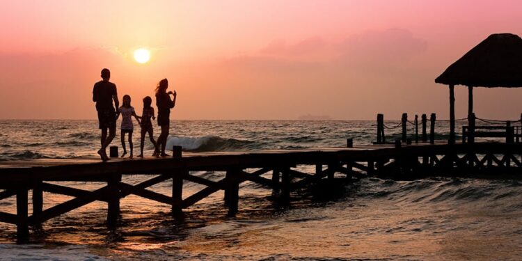 Silhouetted family enjoys a stroll on the beach pier at a vibrant sunset over the ocean waves.