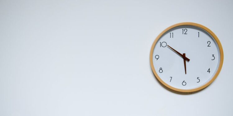 Simple wall clock with wooden frame against a white background, showing the time 10:10.